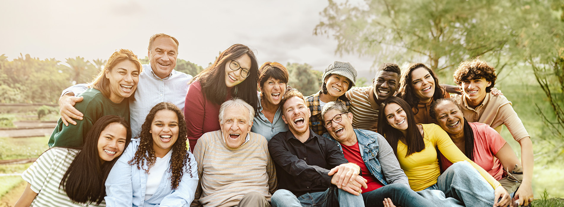 The image shows a group of people sitting together on a bench outdoors, posing for a photograph with smiles on their faces.