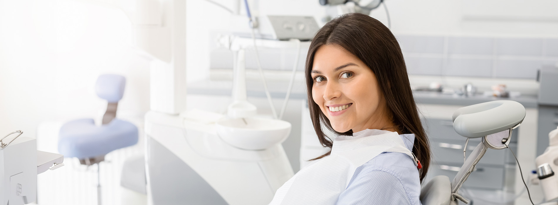 The image shows a woman standing in front of dental equipment with a smile on her face, wearing a white lab coat and stethoscope around her neck.