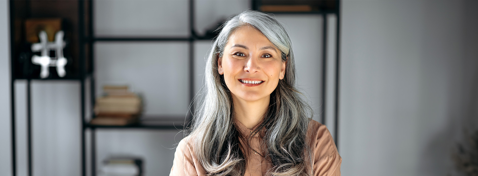 The image features a smiling woman with gray hair, standing indoors against a blurred background, possibly in front of shelves or a display area.