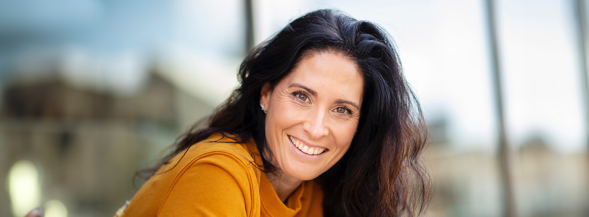 The image shows a woman with brown hair smiling at the camera  she s wearing an orange top and appears to be indoors.