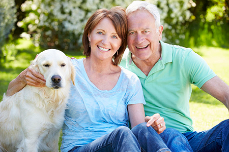 An elderly couple sitting outdoors with their golden retriever.